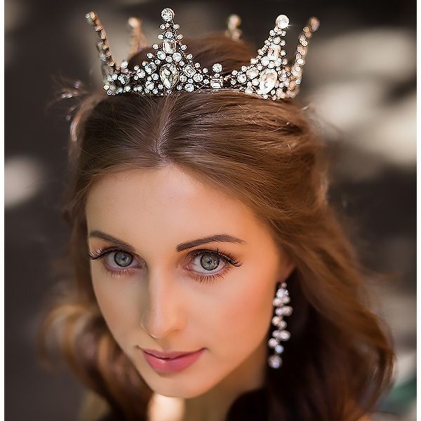 This wedding crown provides a timeless elegance. This is a metal crown that is bronze in colour, and is encrusted in large clear gemstones. The crown is fully rounded and has peaks in its design that add an impressive height and added flair.
